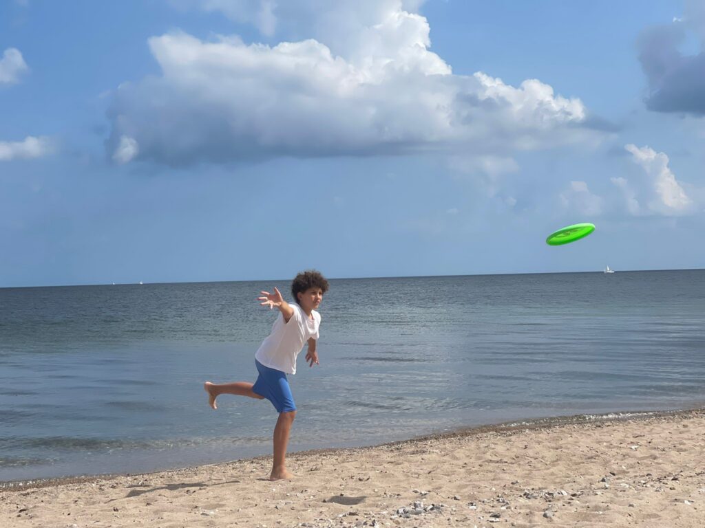 Junge spielt mit einer Frisbee am Meer. Im Englisch Camp der camps for friends.